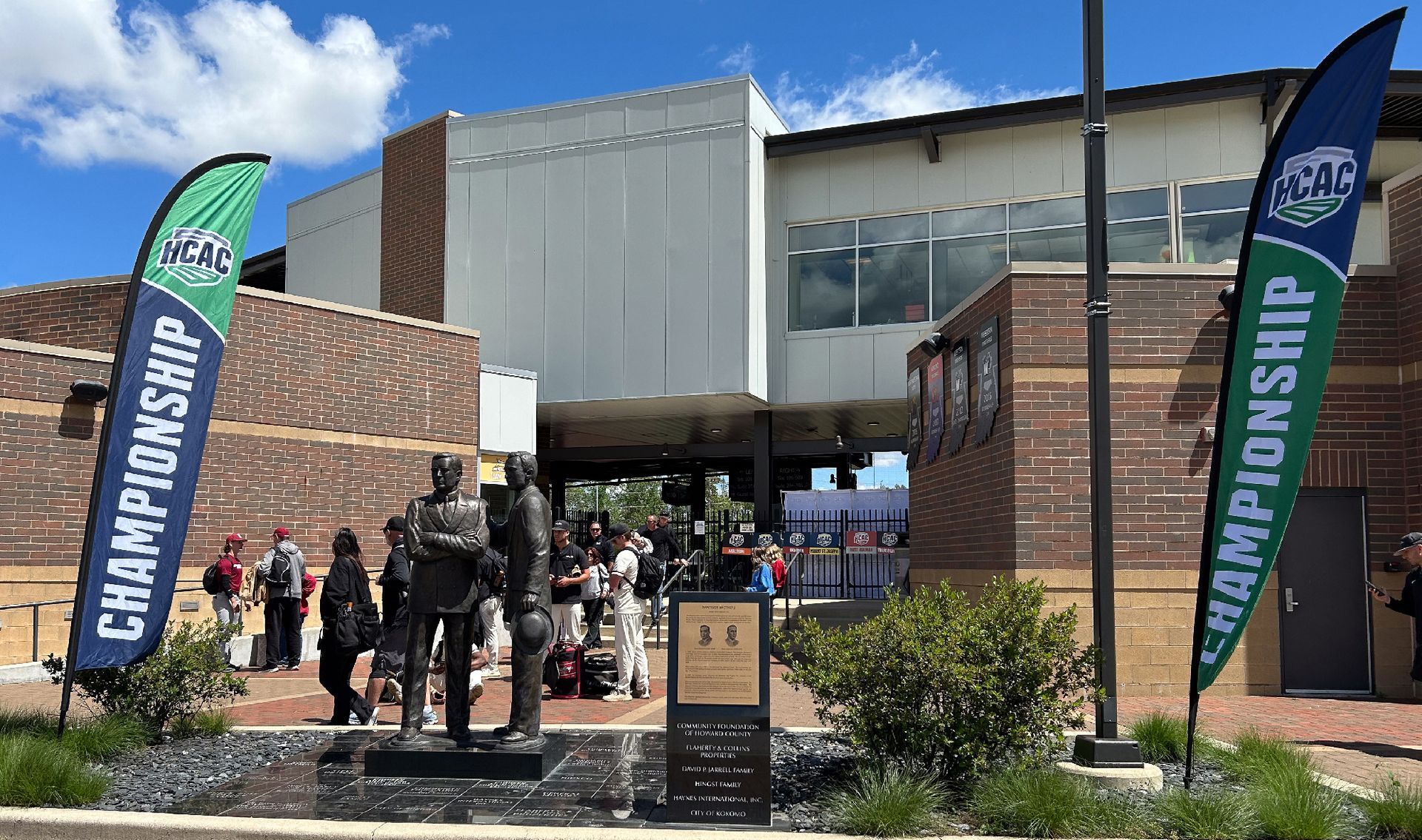 Crowd outside building entrance with blue and green Championship banners on a sunny day