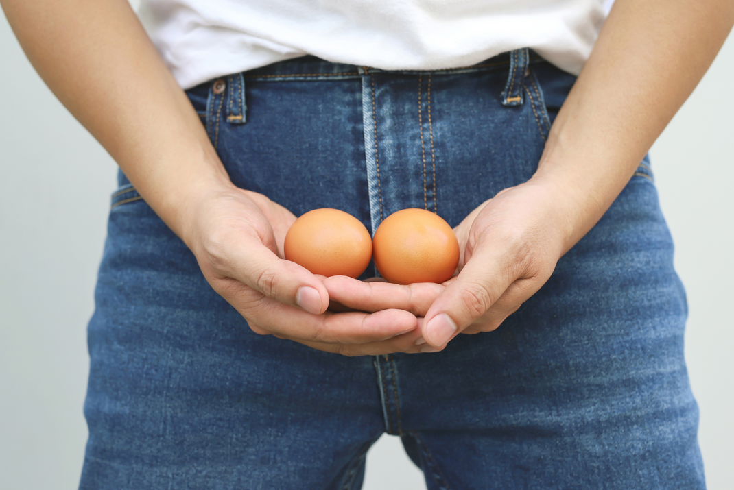 A man is holding two eggs in his hands in front of his pants.