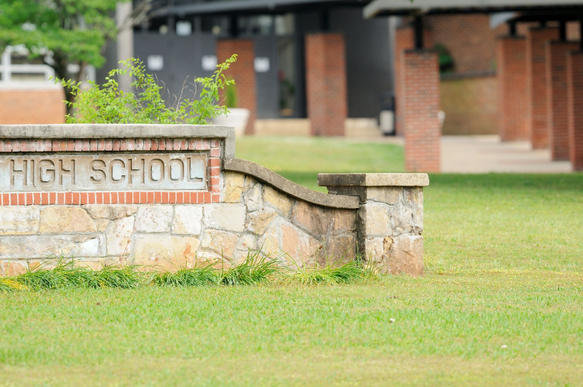 A stone sign with the words High School in front of a grassy area and brick columns A stone sign with the words High School in front of a grassy area and brick columns