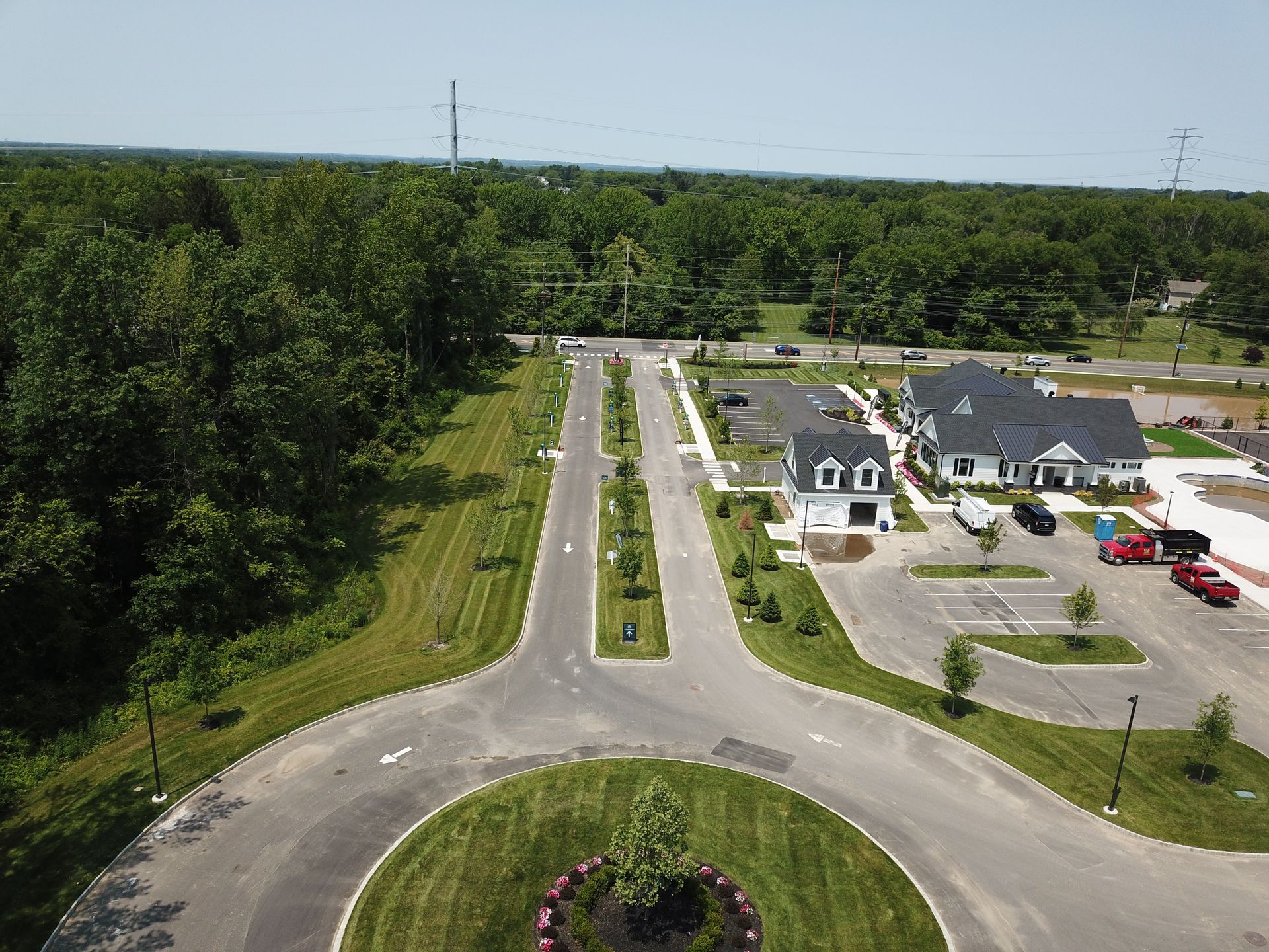 Aerial view of a paved road with a roundabout, leading to a building and parking lot, surrounded by greenery.