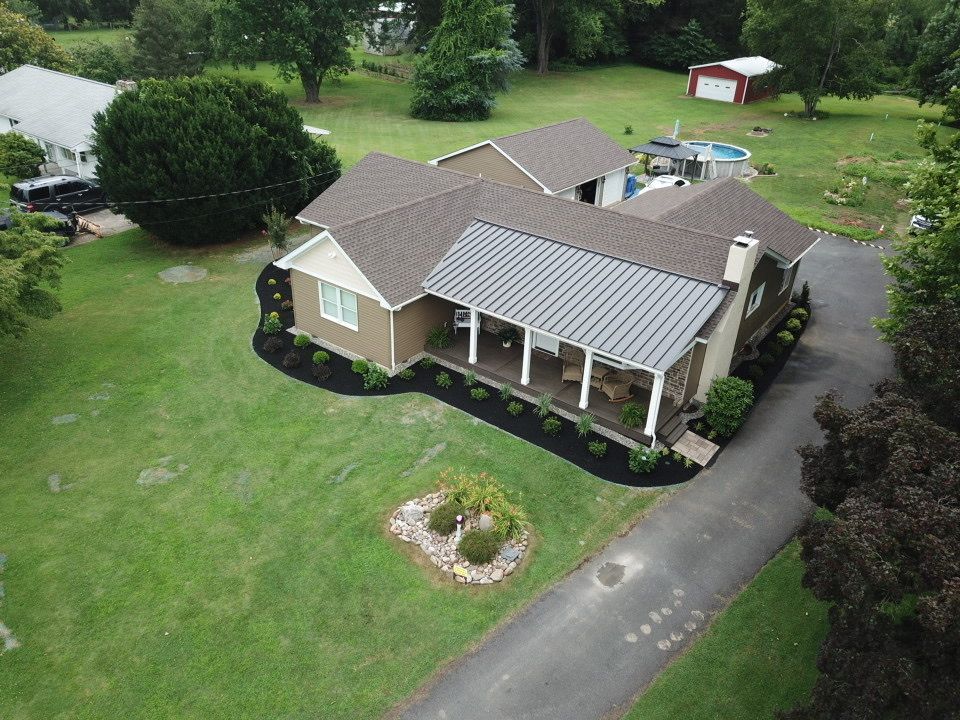 Aerial view of a brown and white house with a metal roof and a long driveway.