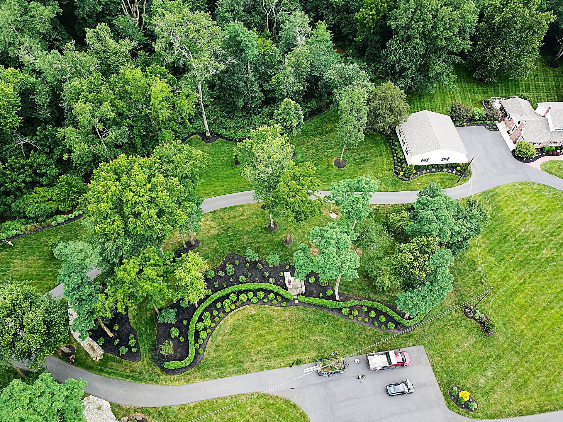 Overhead view of a lush green landscape with trees, a winding pathway, and a white building.
