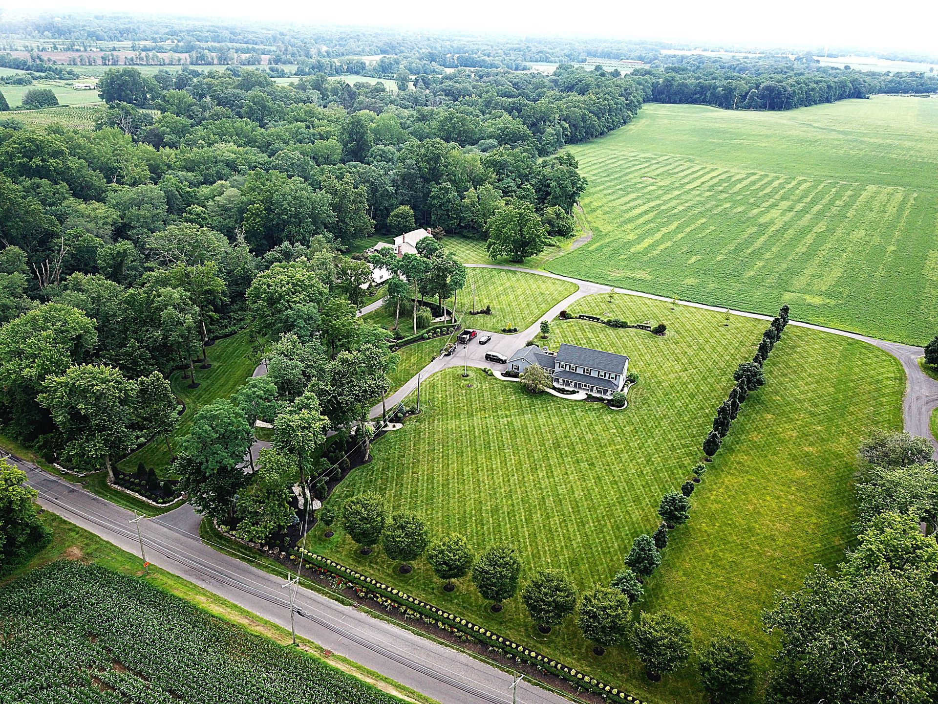 Aerial view of a large house on a green lawn, surrounded by trees and farmland.