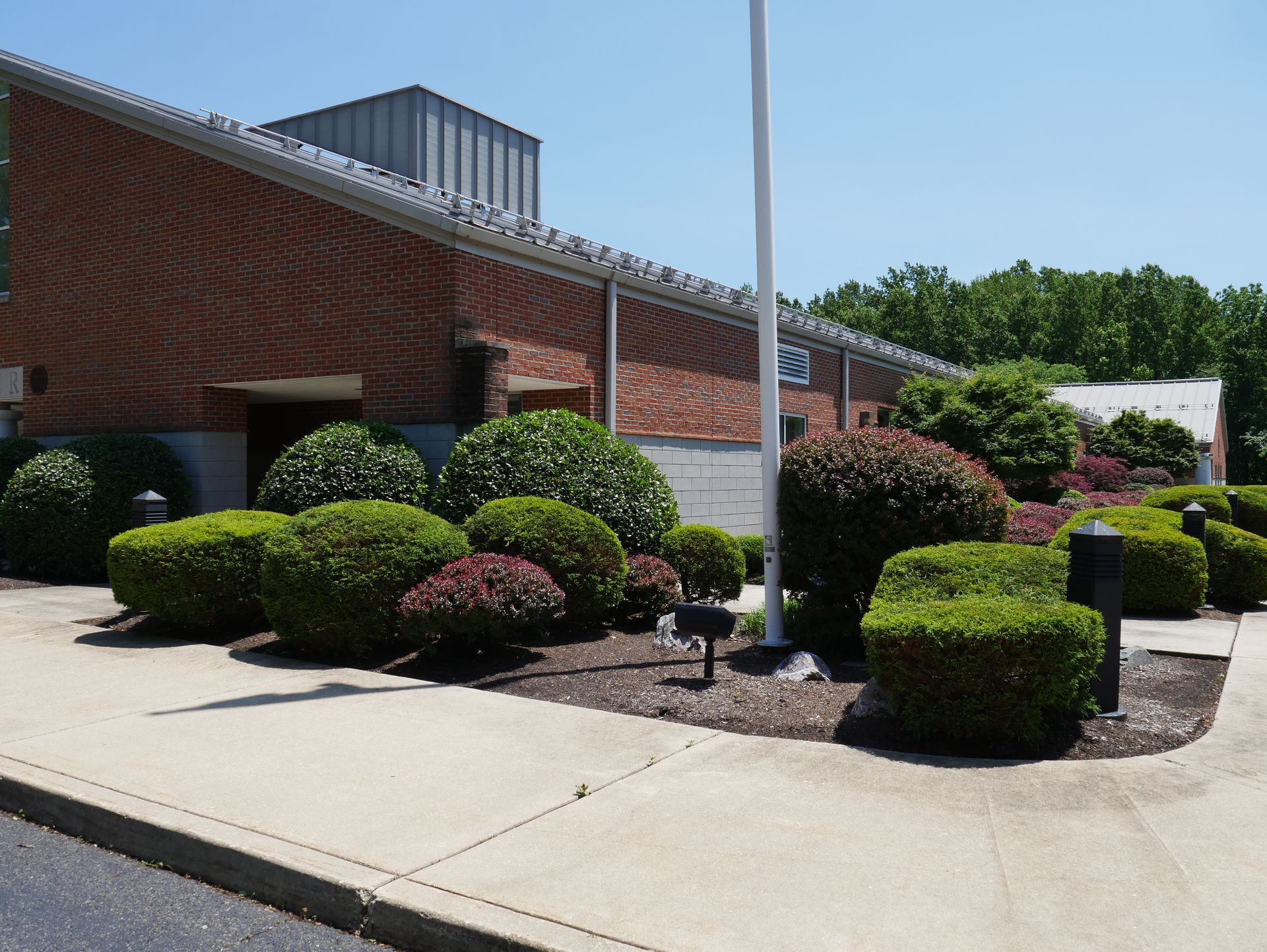 Brick building with trimmed bushes in front; a sunny day.