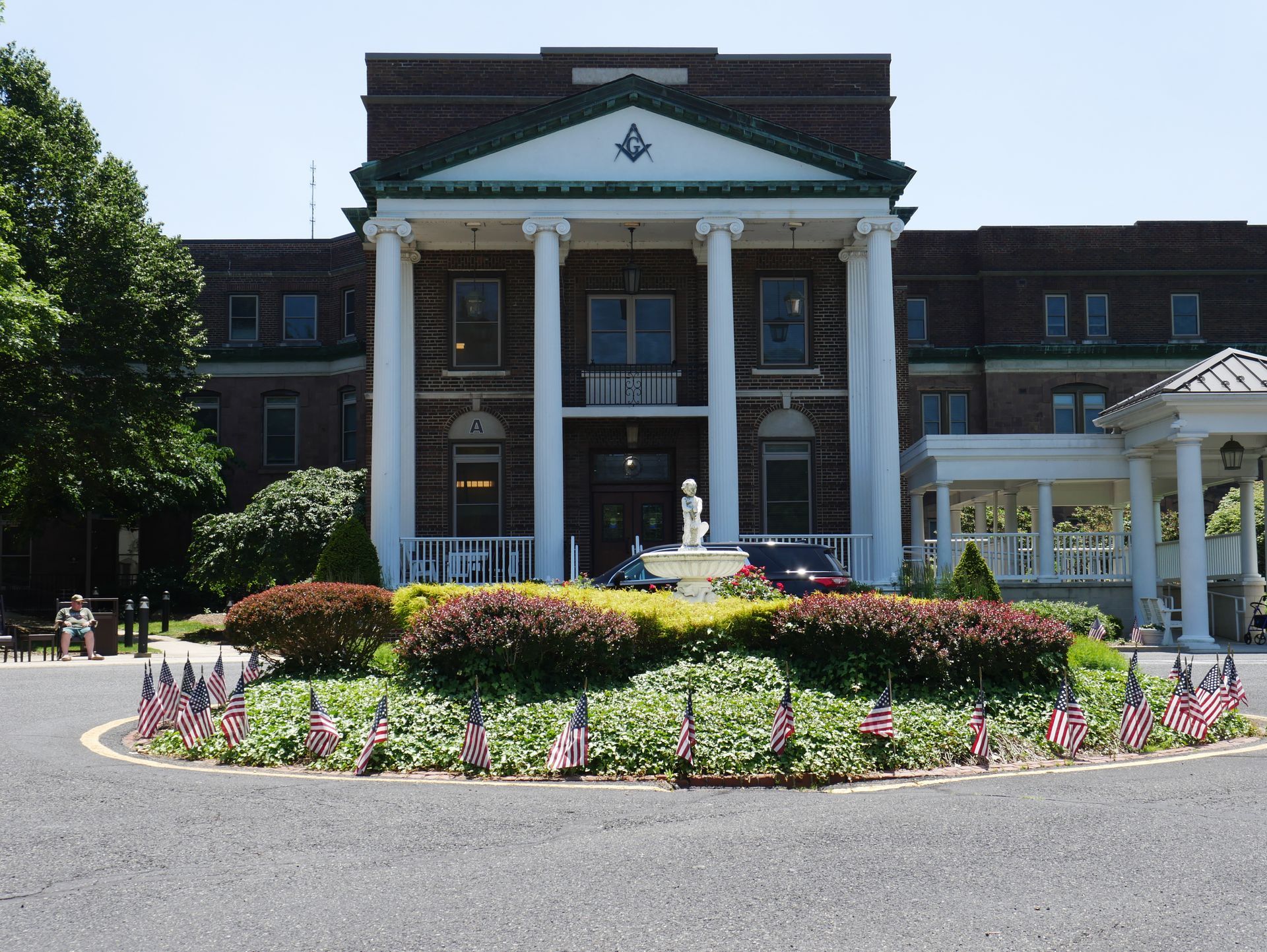 Brick building with white columns, flowerbeds, and a fountain.