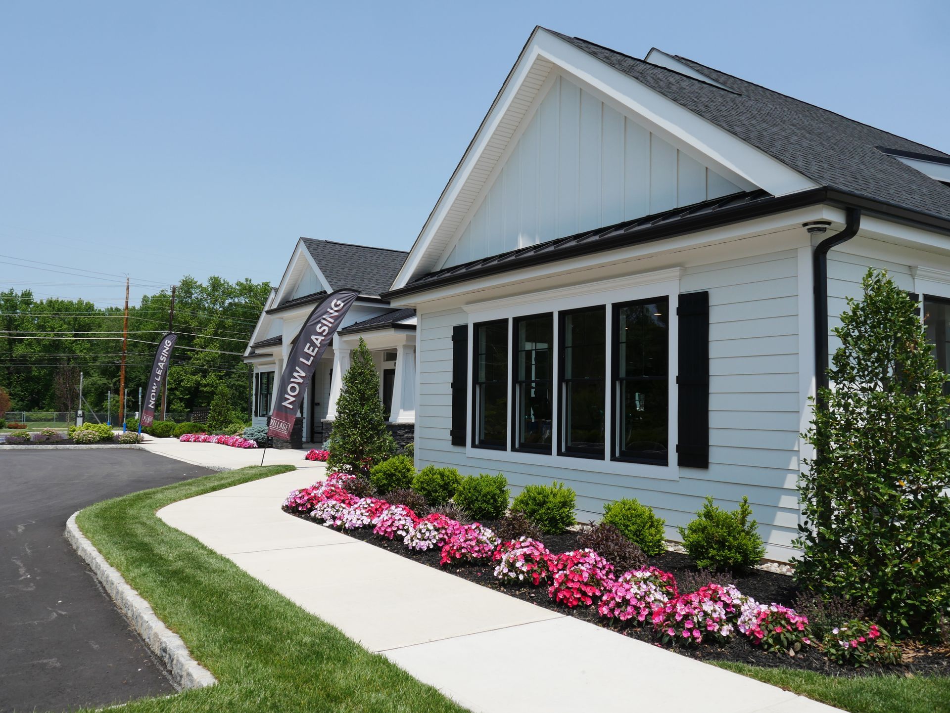 White building with black trim, windows, and roof. Pink and white flowers border a walkway.