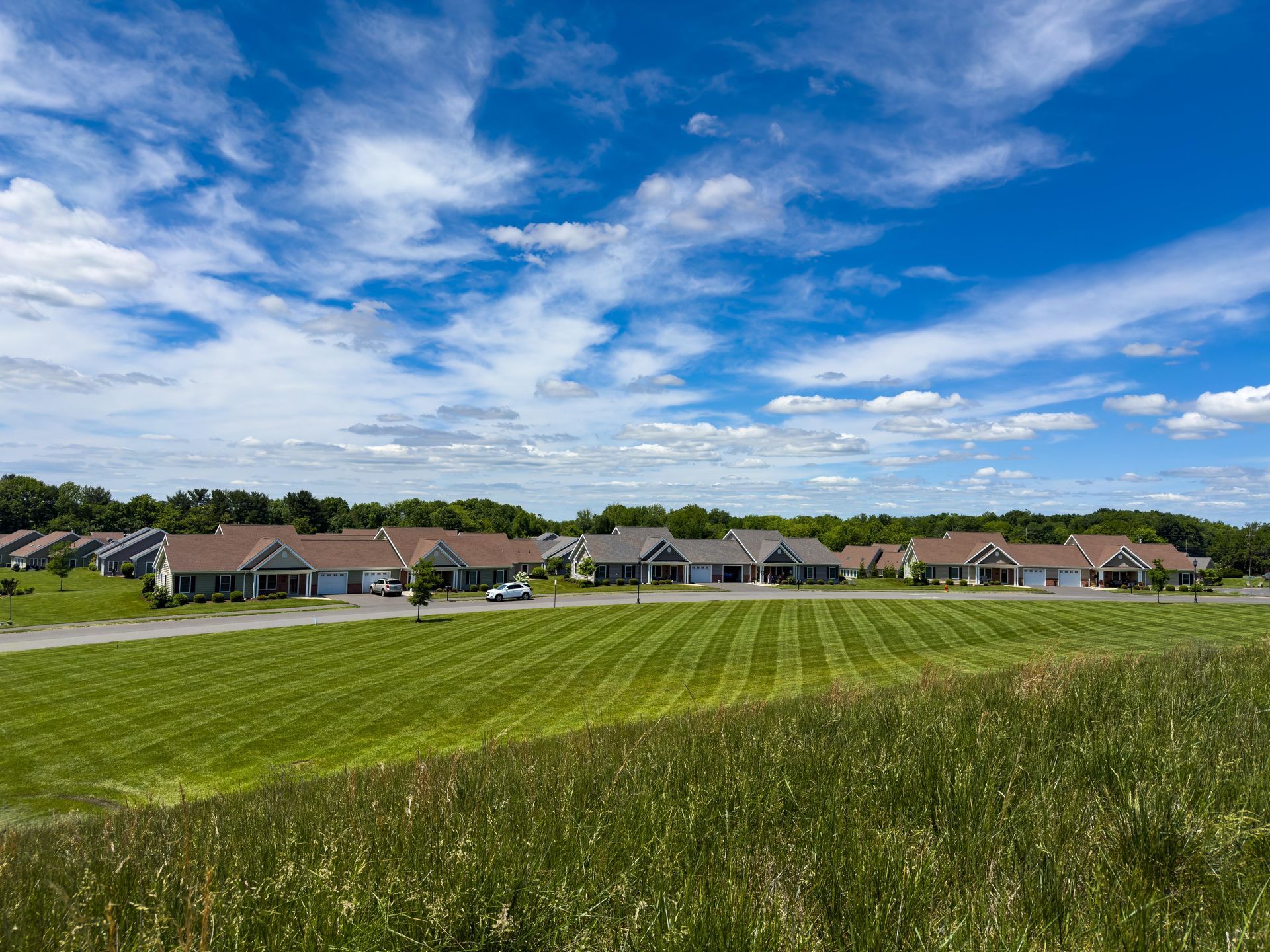 Row of houses with attached garages on a grassy hill under a blue sky with clouds.