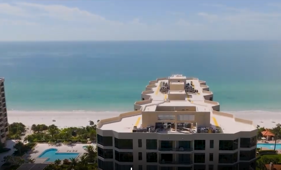 Oceanfront resort building with a rooftop pool overlooking a turquoise beach and calm sea