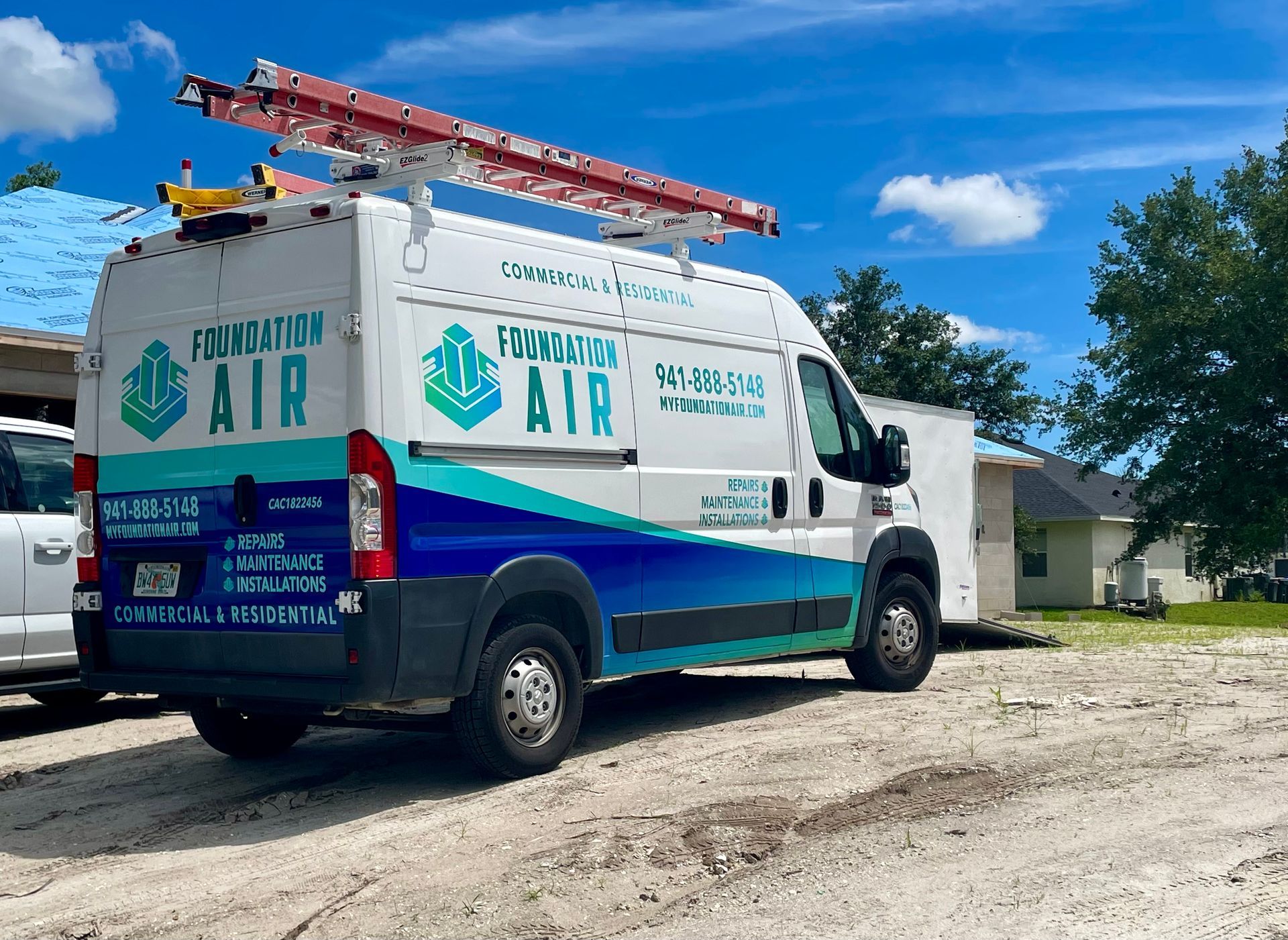 White and blue service van with ladder parked on gravel under a bright blue sky