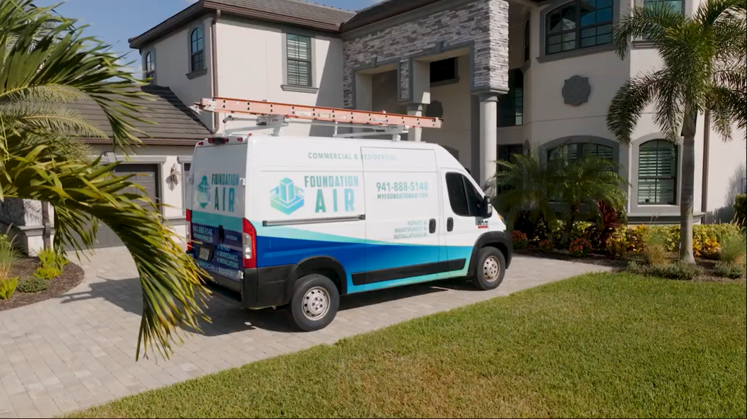 White and blue service van parked on a driveway in front of a house with palm trees.
