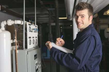 Man in blue shirt taking notes beside industrial control equipment in a factory setting