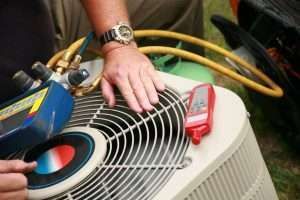 Technician inspecting an outdoor air conditioner unit with yellow hoses attached
