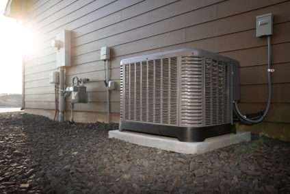 Outdoor home HVAC unit beside beige siding and utility meters on a gravel foundation