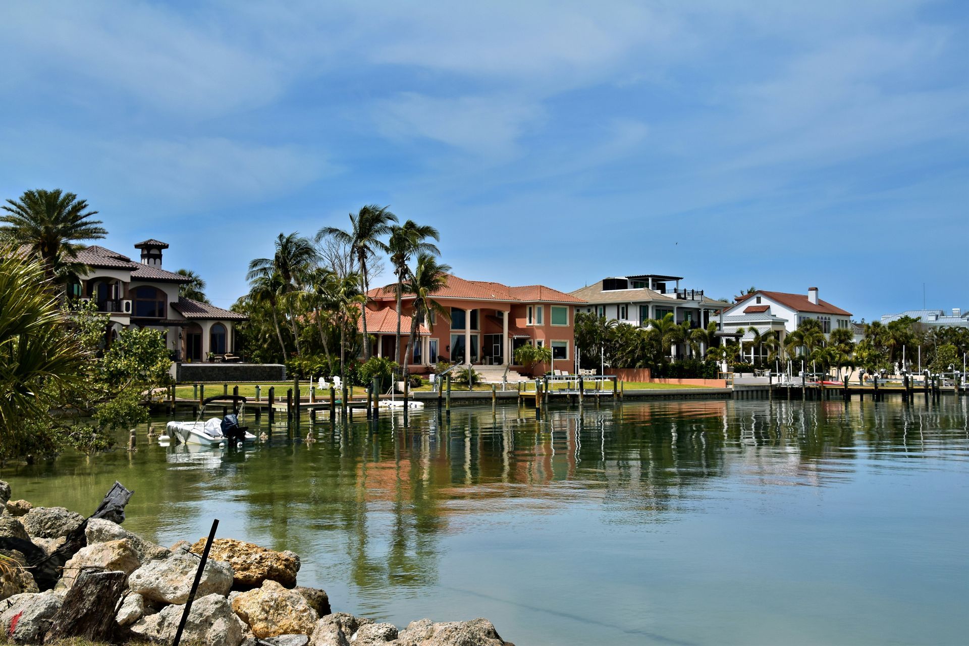 Waterfront homes with palm trees reflected in a calm canal under a blue sky