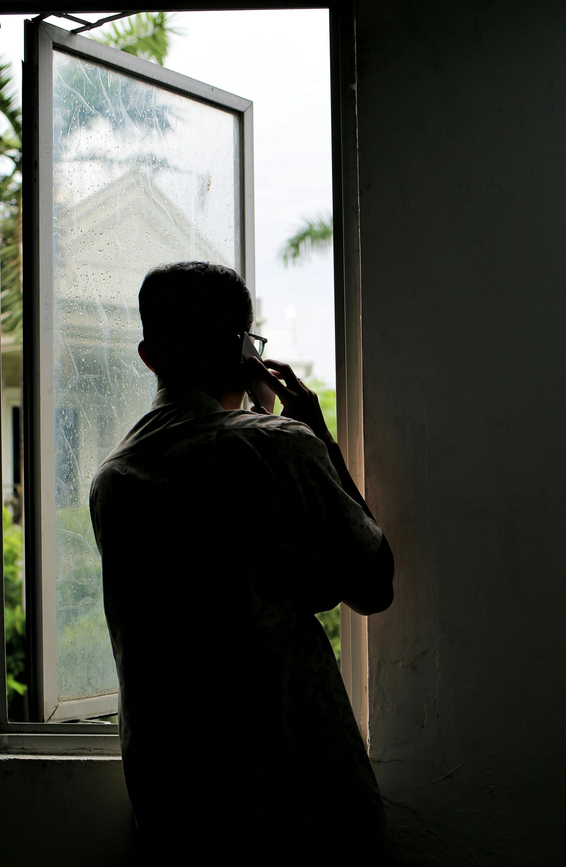Silhouette of a person by an open window, looking outside into daylight.
