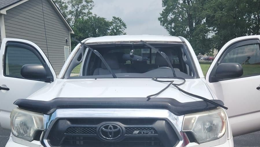 White Toyota Tacoma truck with open doors, damaged windshield, and a bug deflector.