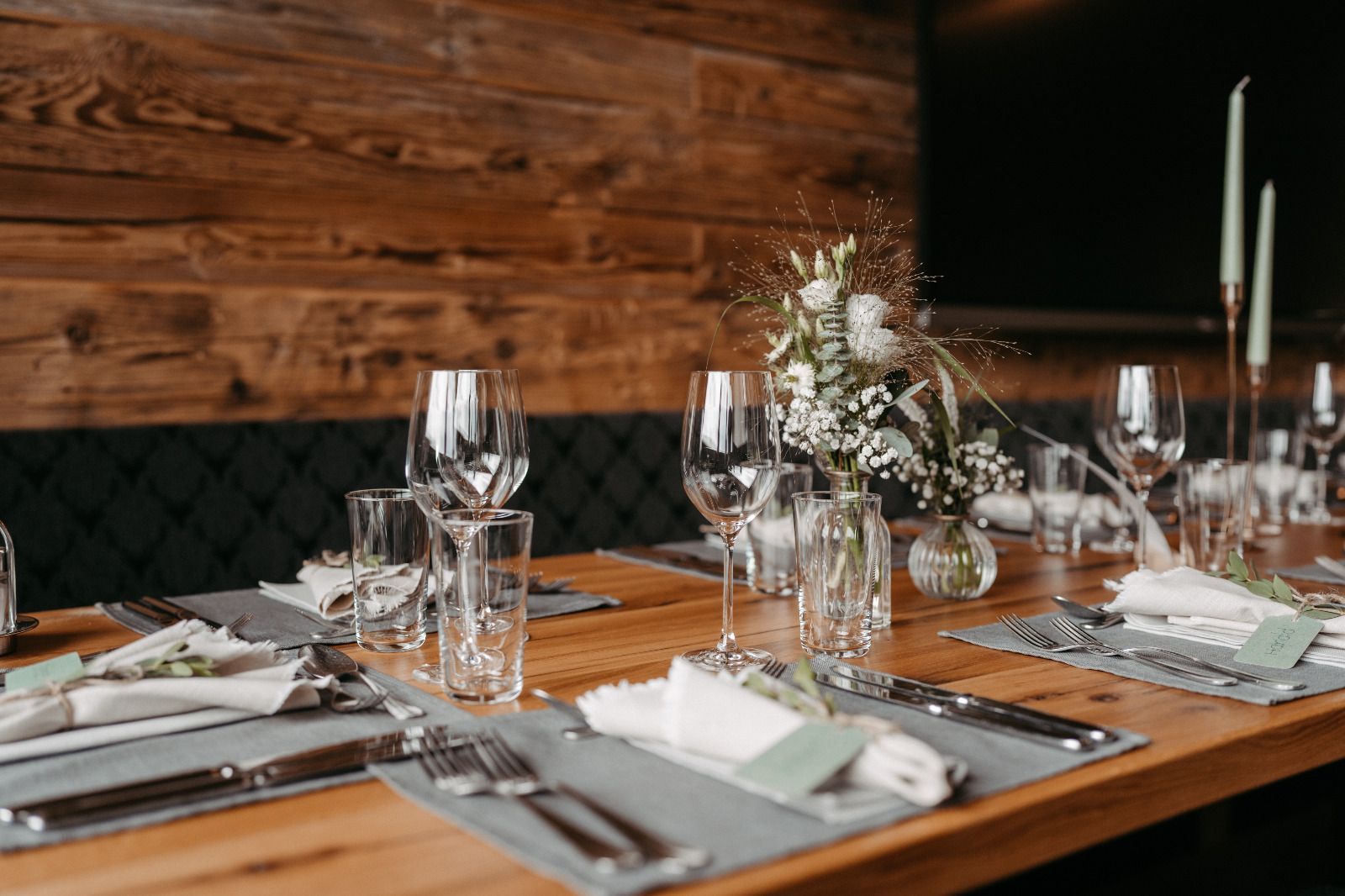 Ein Holztisch mit Gläsern, Besteck und Blumen darauf.