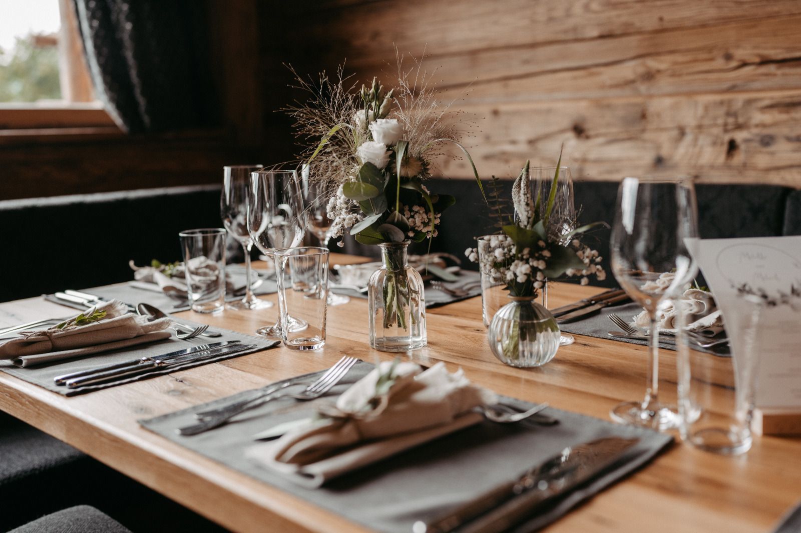 Ein Holztisch mit Tellern, Servietten, Gläsern und Blumen darauf.