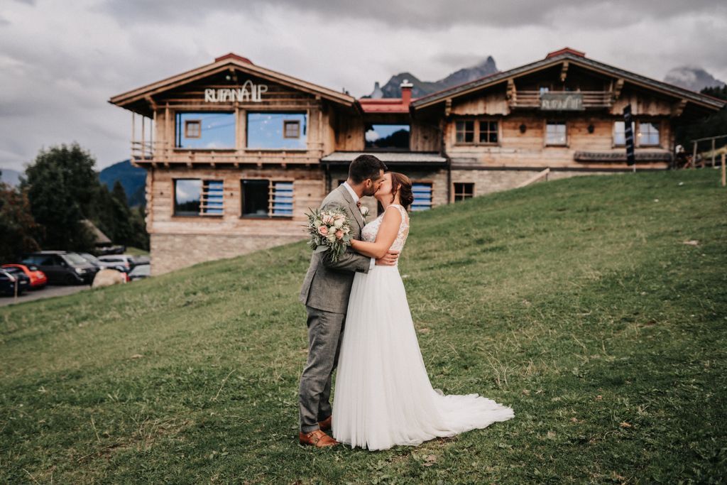 Eine Braut und ein Bräutigam küssen sich vor einem großen Holzgebäude.
