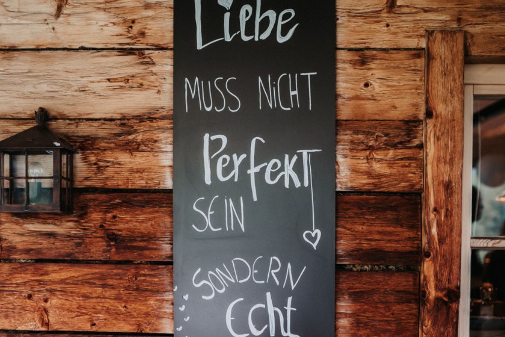 A blackboard with the words `` liebe muss nicht perfekt sein '' written on it is hanging on a wooden wall.