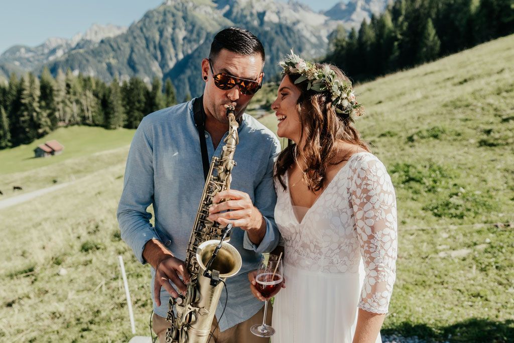 Ein Mann spielt Saxophon neben einer Frau, die ein Glas Wein hält.