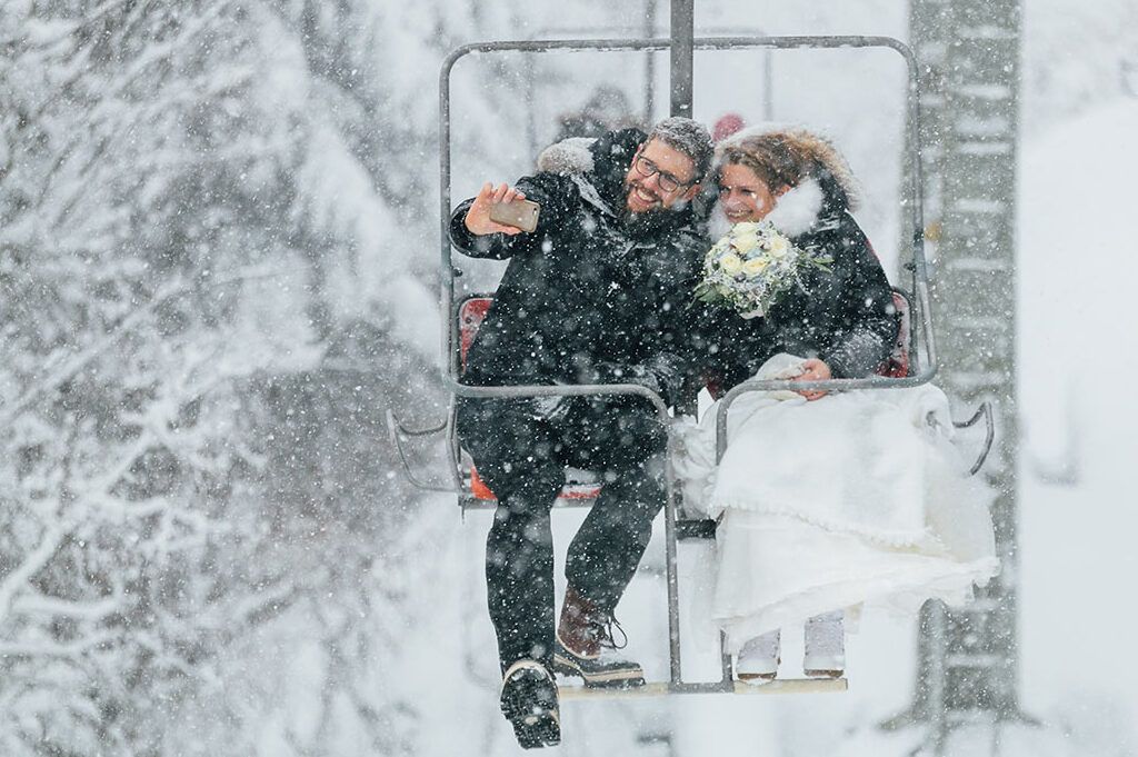 Eine Braut und ein Bräutigam fahren mit einem Skilift im Schnee.