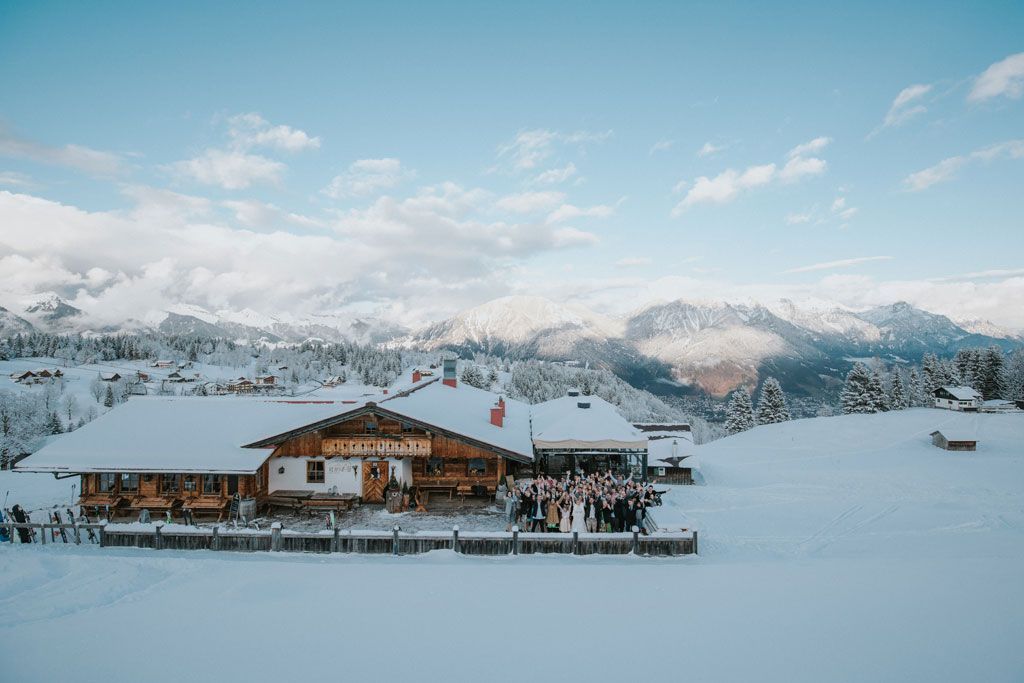 Eine Gruppe von Menschen steht vor einer schneebedeckten Hütte in den Bergen.