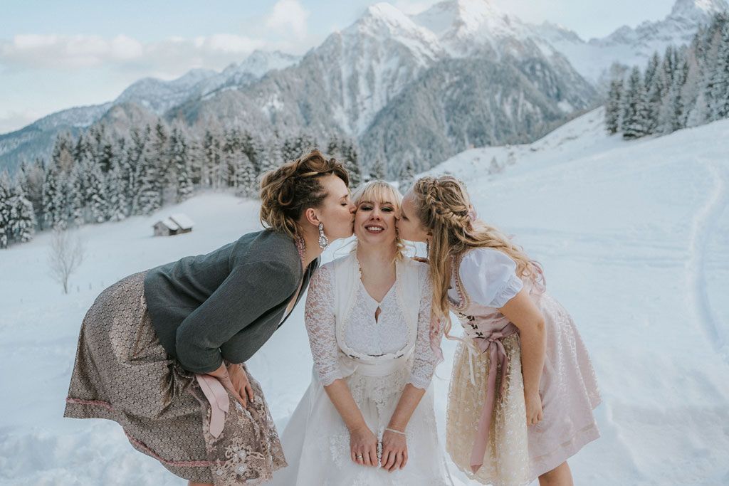 Zwei Frauen küssen eine Braut im Schnee auf die Wange.