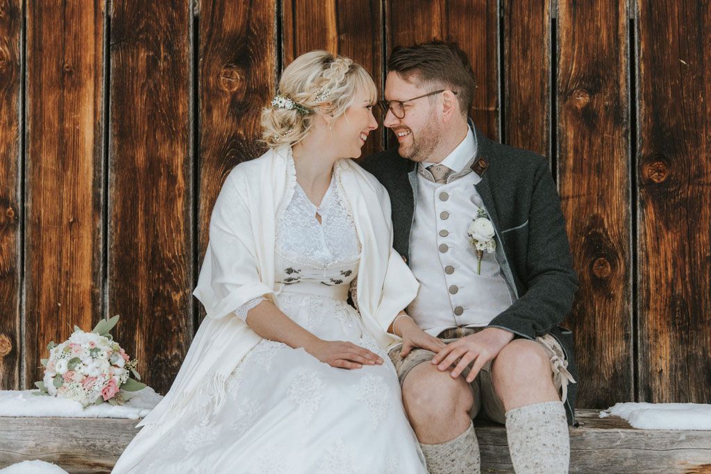 Eine Braut und ein Bräutigam sitzen auf einer Bank und schauen einander an.