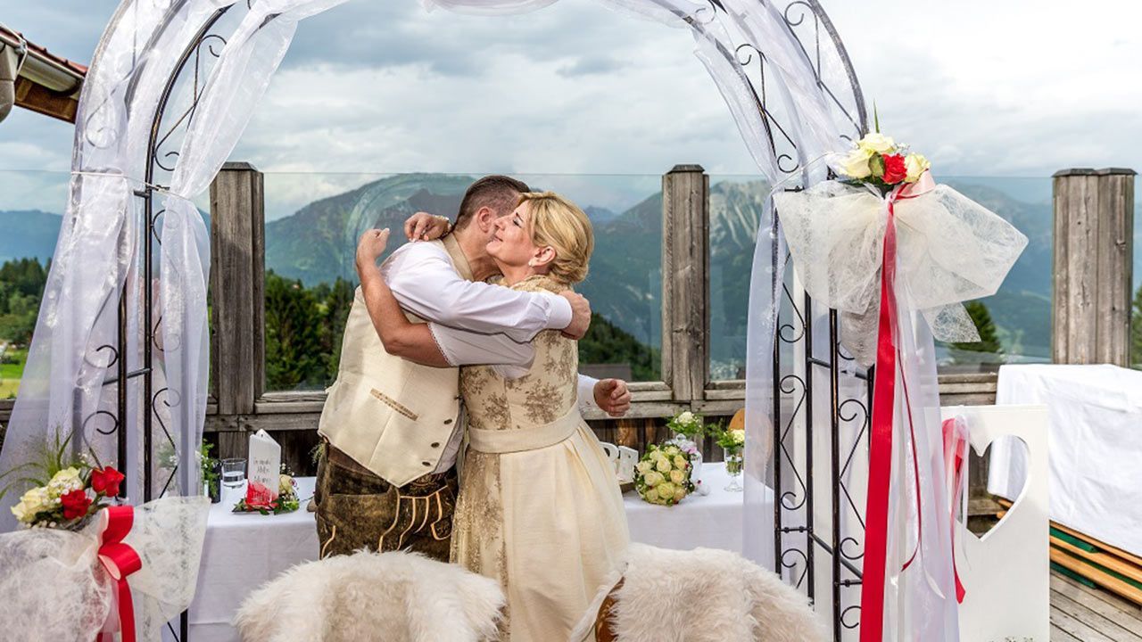 Eine Braut und ein Bräutigam küssen sich bei ihrer Hochzeitszeremonie unter einem Bogen.