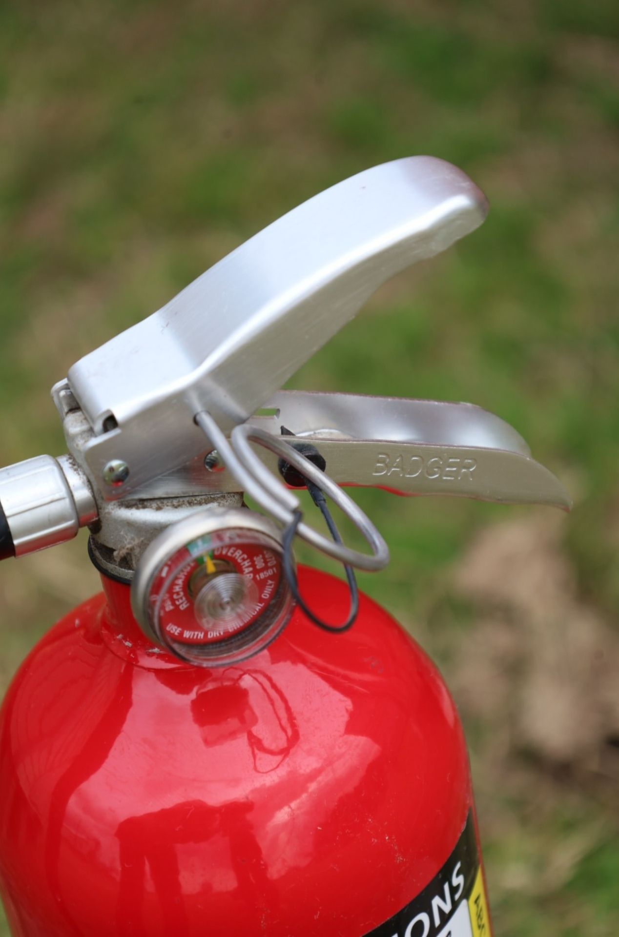 Close-up of a red fire extinguisher with a silver handle, pressure gauge, and safety pin.