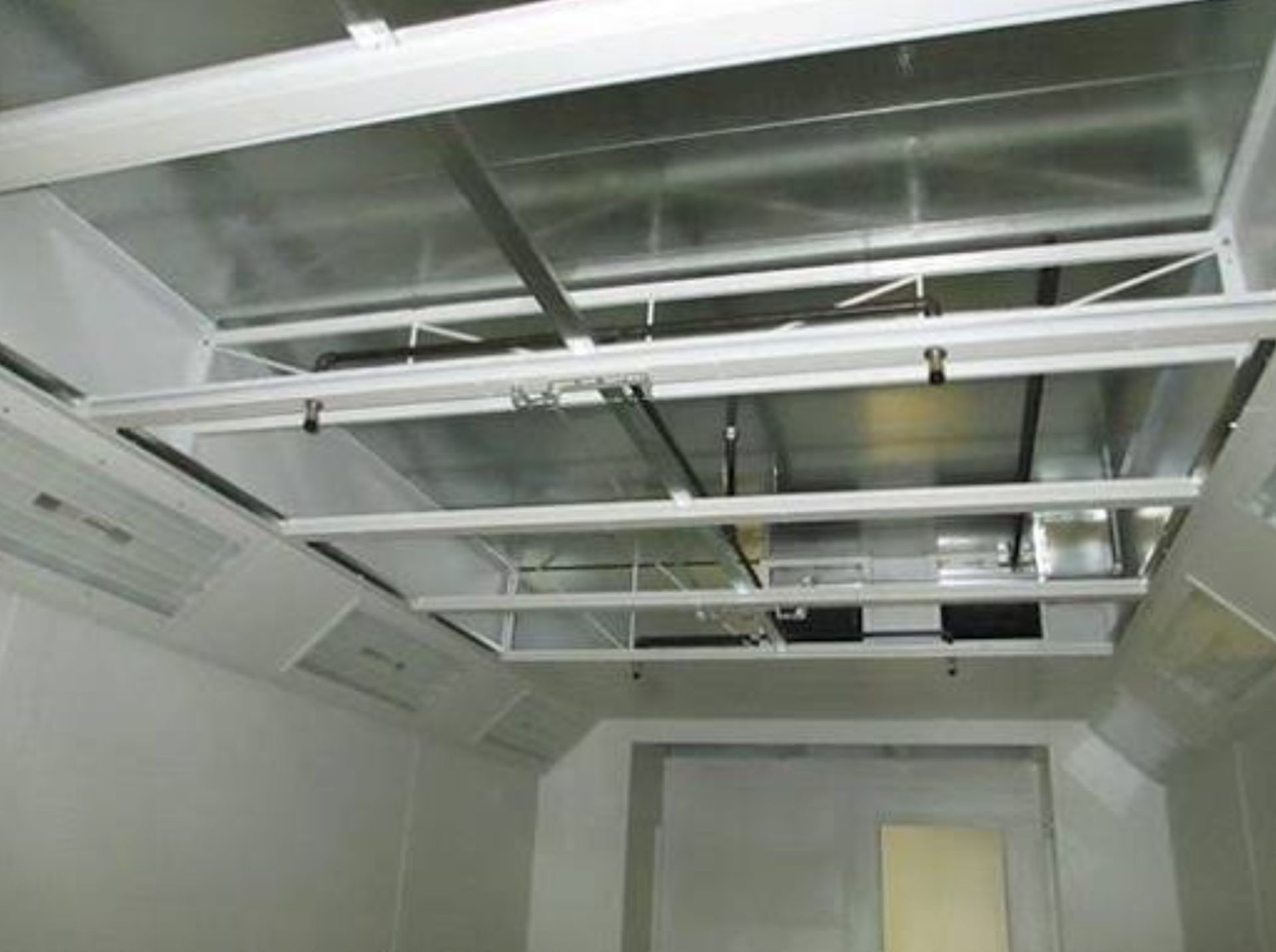 Interior of a spray booth; white walls and ceiling with overhead metal framework and lighting.