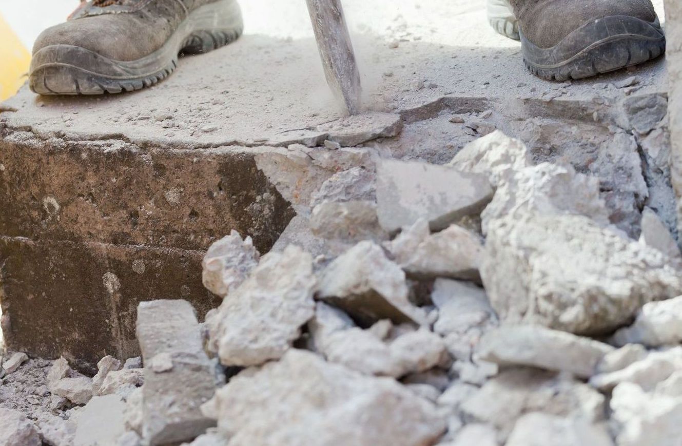 man demolishing concrete surface by jackhammering the concrete away