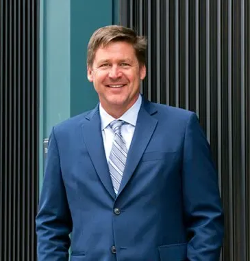 Smiling man in blue suit and striped tie standing in front of a modern building.