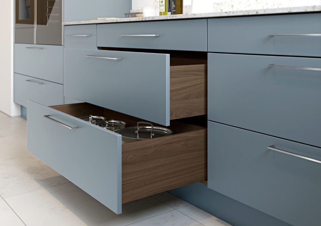 A kitchen with blue cabinets and a wooden drawer open.