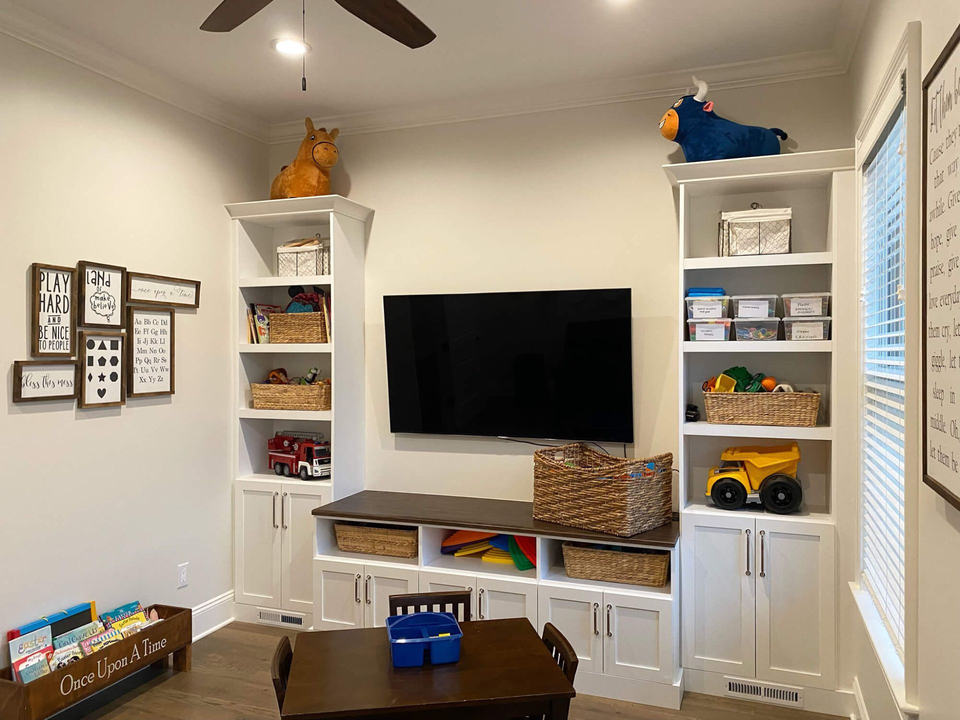 A play room with a table , shelves , and a flat screen tv.