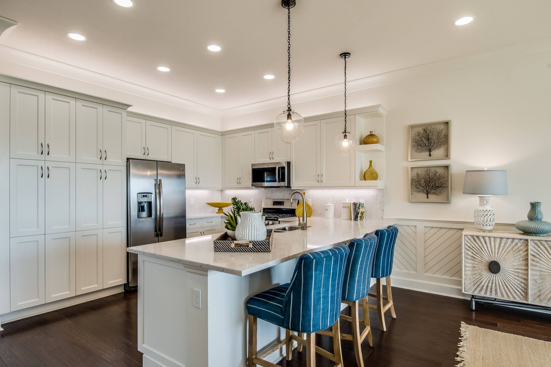 A kitchen with white cabinets , stainless steel appliances , a large island , and blue chairs.