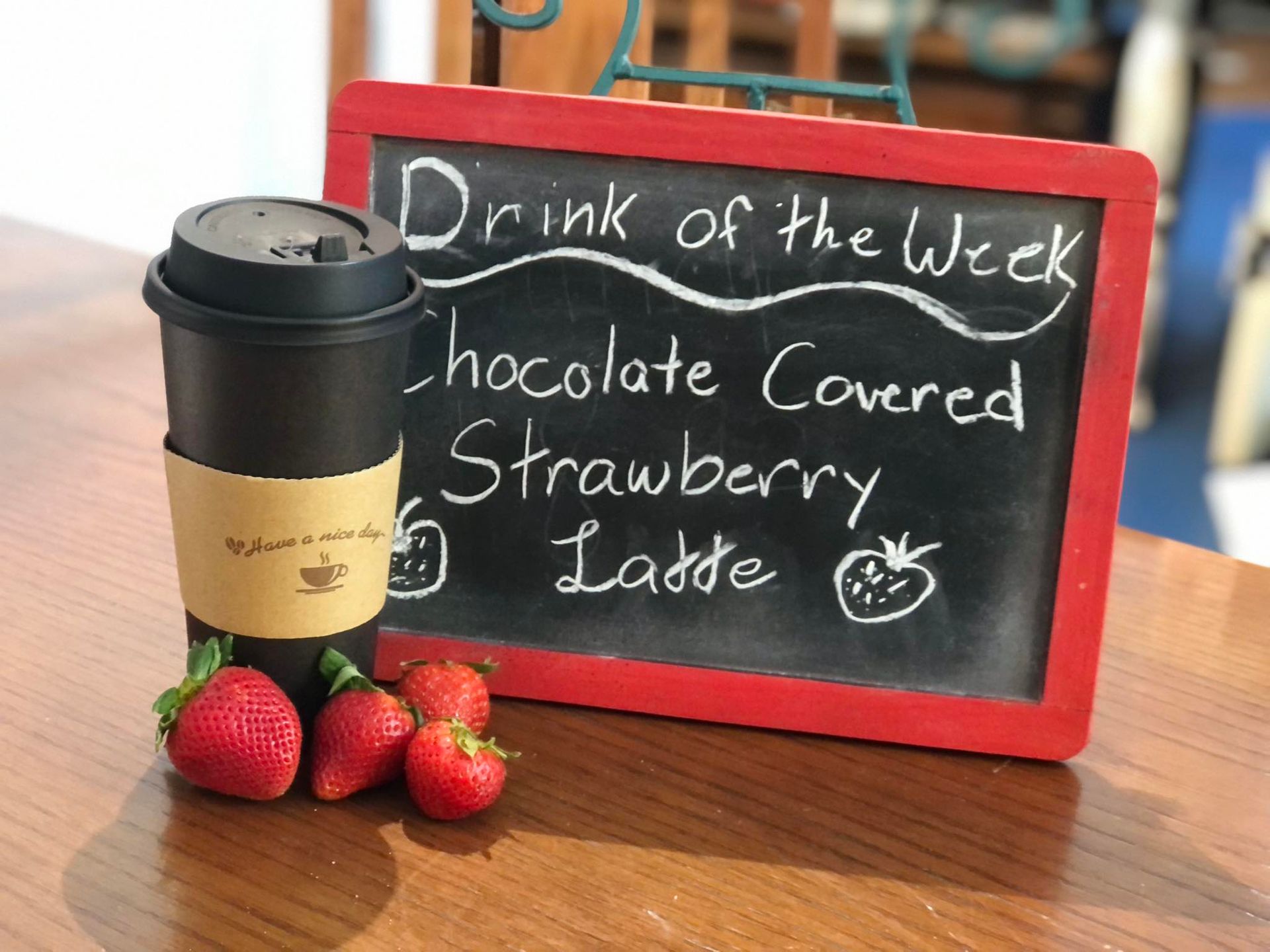 A cup of chocolate covered strawberry latte is on a table next to strawberries