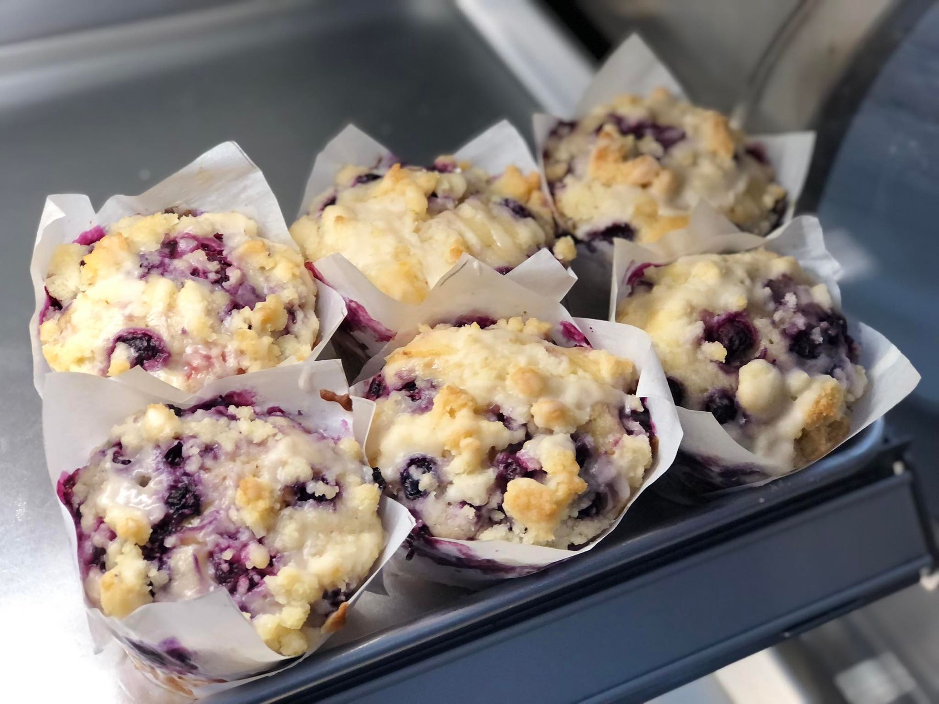 A bunch of blueberry muffins are sitting on a metal tray.