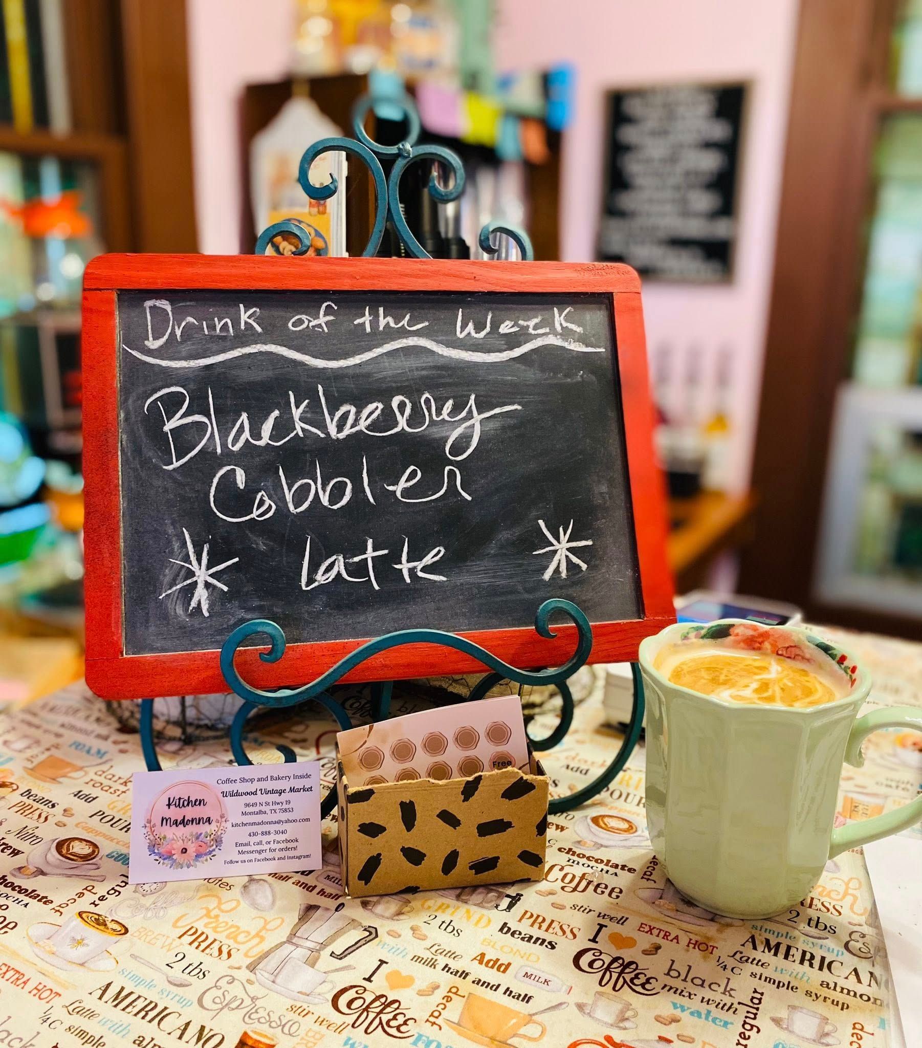 A cup of coffee is sitting on a table next to a sign that says drink of the week.