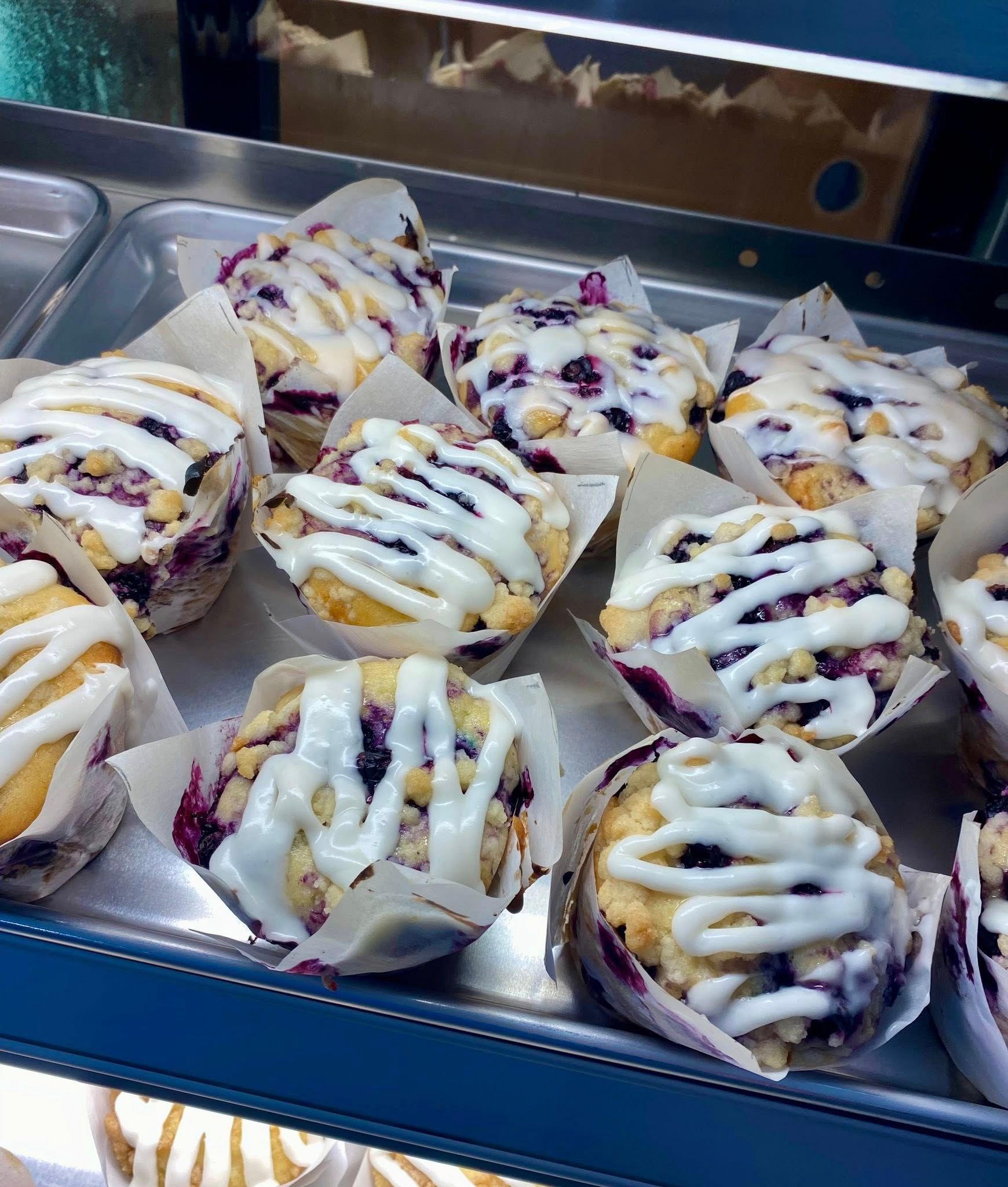 A tray of blueberry muffins with white frosting on them