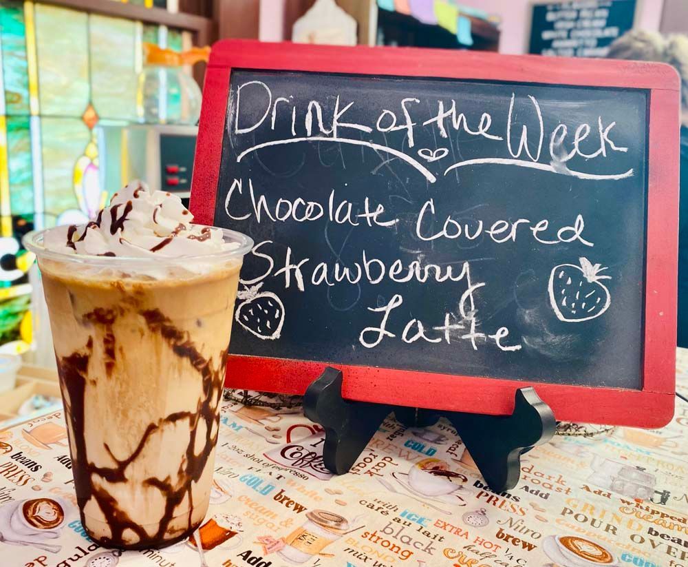 A drink of the week chocolate covered strawberry latte is on a table.