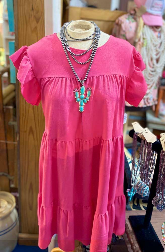 A pink dress with ruffled sleeves and a turquoise necklace on a mannequin.