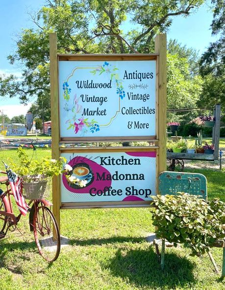 A sign for a kitchen madonna coffee shop is sitting in the grass next to a bicycle.