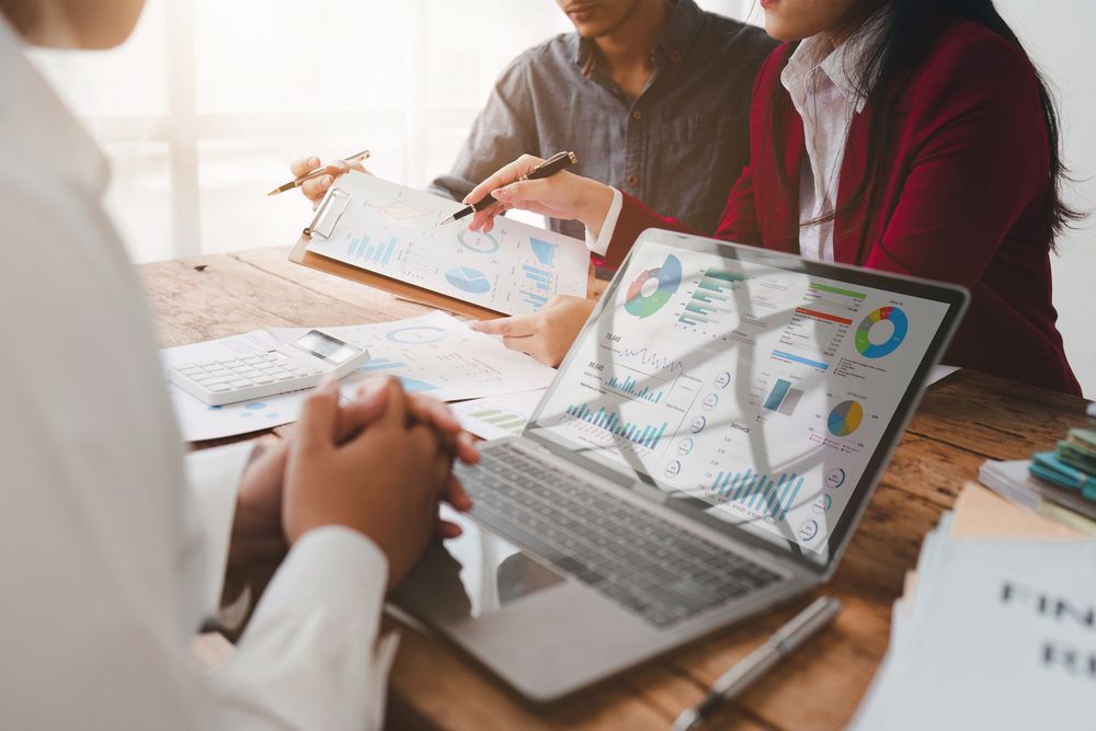 A Group Of People Are Sitting At A Table Looking At A Laptop Computer — Wagga Tradesman Accounting Services In Wagga Wagga, NSW