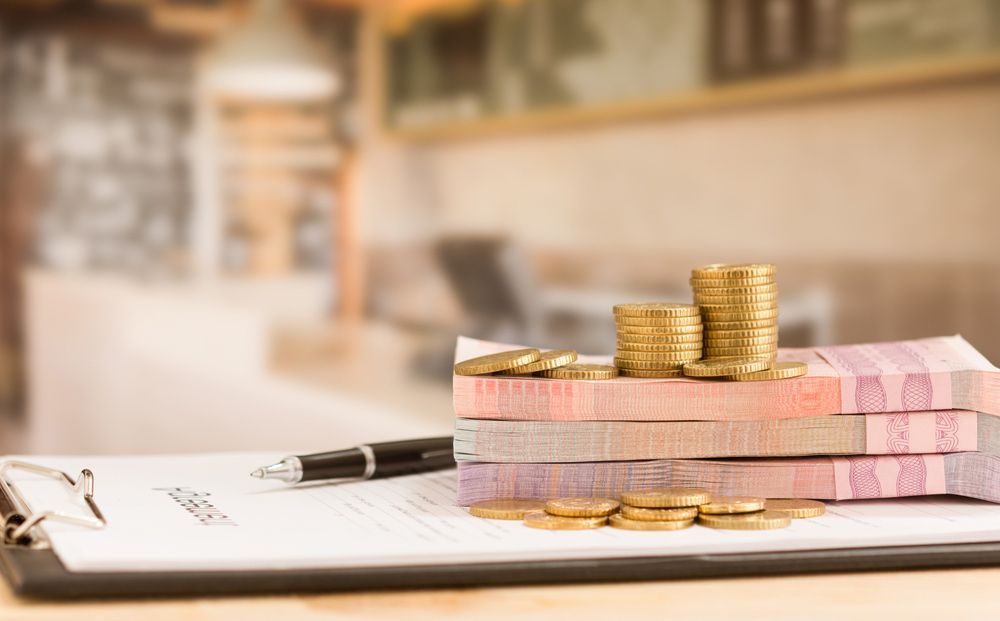 A Clipboard With Stacks Of Money And Coins On It — Wagga Tradesman Accounting Services In Wagga Wagga, NSW