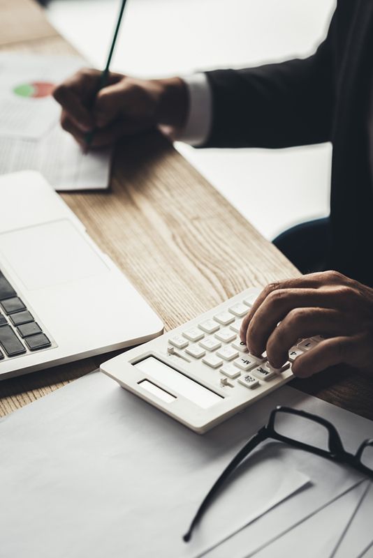 A Man Is Using A Calculator While Writing On A Tablet — Wagga Tradesman Accounting Services In Wagga Wagga, NSW