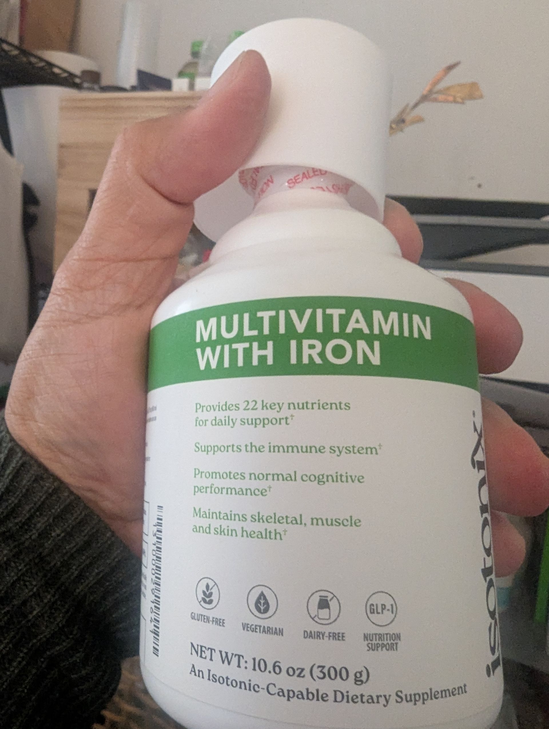 Hand holding a white bottle of multivitamin with iron. The bottle has green text on it.