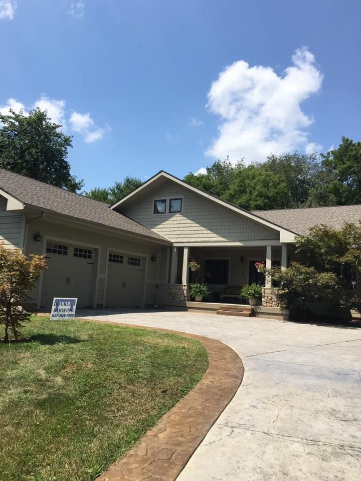 A ranch-style house with a two-car garage and a curved driveway on a sunny day.