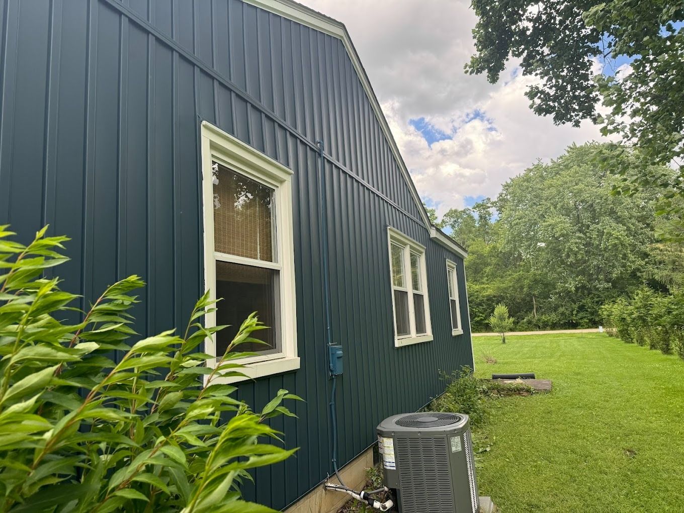 Blue sided house with white trim windows, air conditioner, and green lawn.